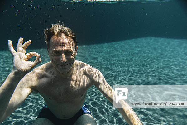 Porträt eines lächelnden Mannes unter Wasser in einem Swimmingpool mit ok-Schild