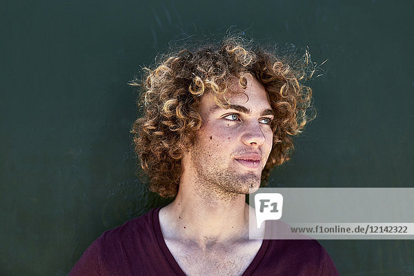 Porträt eines lächelnden jungen Mannes mit lockigen Haaren vor einer grünen Wand