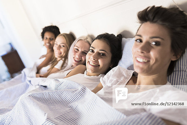 Portrait of smiling female friends lying in bed side by side