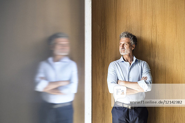 Reflection of mature businessman standing at wooden wall