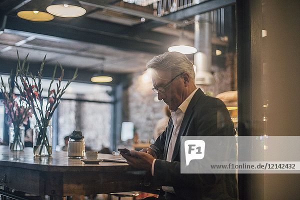 Senior Geschäftsmann sitzt im Cafe  mit Smartphone