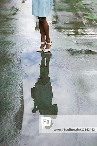 USA  New York  junge Afroamerikanerin auf der Straße stehend  High Heels  Wasserspiegelung in der Pfütze