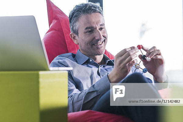 Smiling man sitting in beanbag holding molecule model