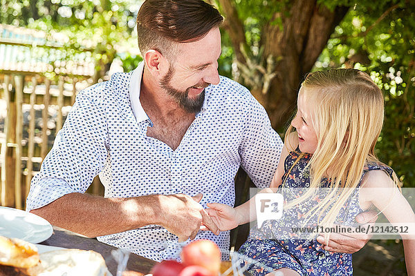 Glückliches Mädchen mit Vater am Gartentisch sitzend