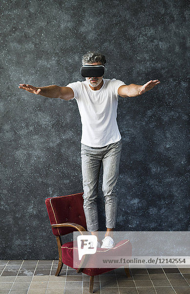 Der reife Mann schaut durch die VR-Brille und balanciert auf dem Sessel.