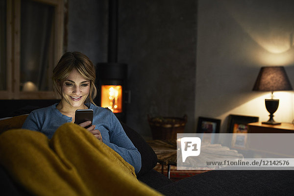 Porträt einer lächelnden Frau mit Smartphone  die sich abends auf der Couch ausruht.