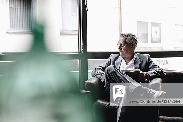 Senior Geschäftsmann sitzt auf dem Stuhl und liest Zeitung.