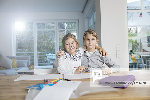 Portrait of two girls embracing doing homework at table together