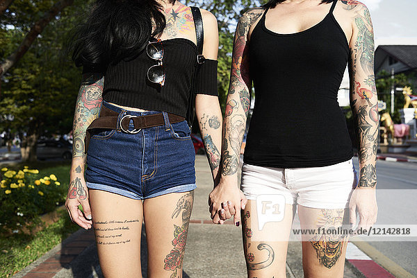 Tätowiertes lesbisches Paar  das im Sommer auf der Straße Händchen hält.