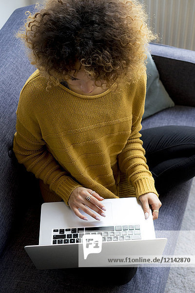 Young woman sitting on couch at home using laptop