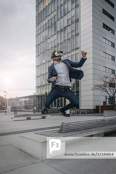 Businessman wearing VR glasses jumping in the city