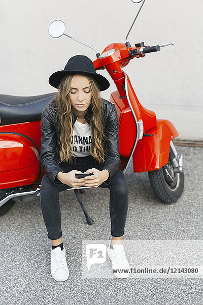 Fashionable young woman with red motor scooter using cell phone