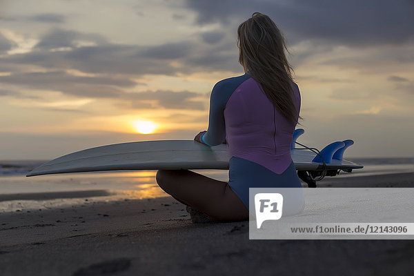 Indonesien  Bali  junge Frau mit Surfbrett am Strand bei Sonnenuntergang