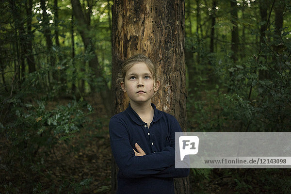 Portrait of confident girl standing at tree trunk in forest