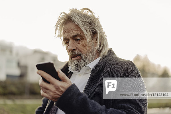 Serious senior man holding cell phone outdoors