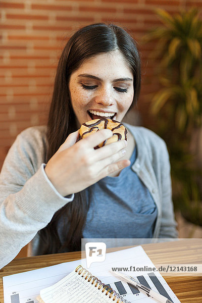 Glückliche Geschäftsfrau beim Essen eines Donuts am Schreibtisch im Büro