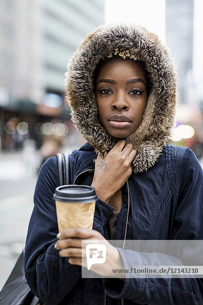 Porträt der modischen jungen Frau mit Kaffee zum Mitnehmen in Kapuzenjacke