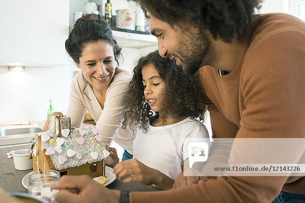 Family pasting gingerbread house in kitchen for Christmas with sweets