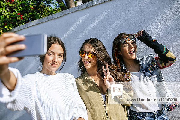 Drei lächelnde junge Frauen nehmen Selfie mit Smartphone