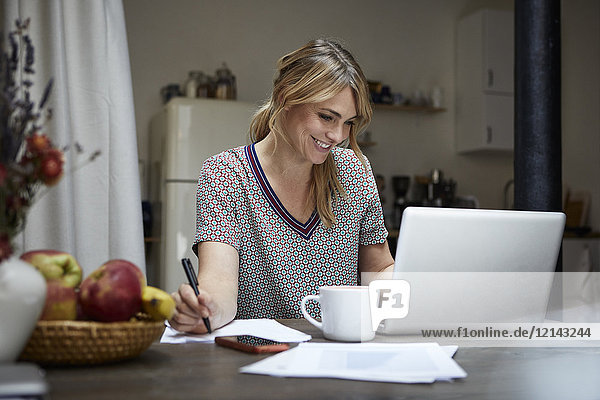 Porträt einer lachenden Frau bei der Arbeit am Laptop zu Hause