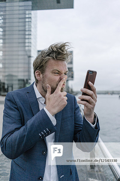 Businessman with cell phone picking nose