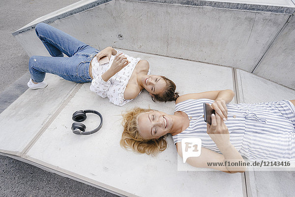 Zwei glückliche junge Frauen mit Handy und Kopfhörer im Skatepark
