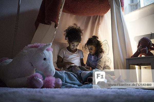 Two sisters sitting in dark children's room  looking at digital tablet