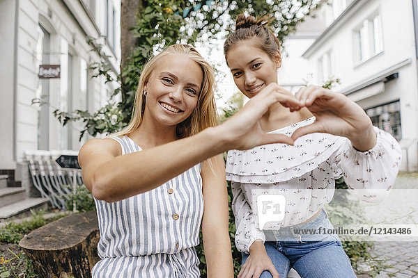Two smiling young women shaping heart with their hands in the city