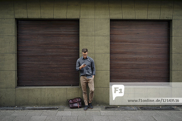 Junger Mann lehnt sich mit dem Handy an die Hausfront