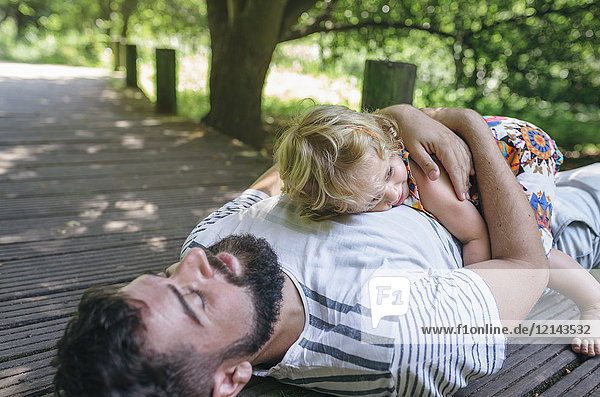 Little girl hugging her father lying on a wooden walkway in the countryside