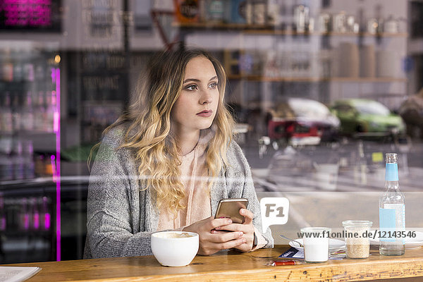 Porträt einer nachdenklichen jungen Frau in einem Café mit Blick durchs Fenster