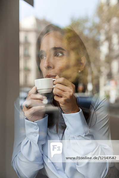Geschäftsfrau trinkt Espresso hinter der Fensterscheibe