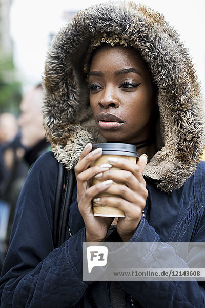 Porträt der modischen jungen Frau mit Kaffee zum Mitnehmen in Kapuzenjacke
