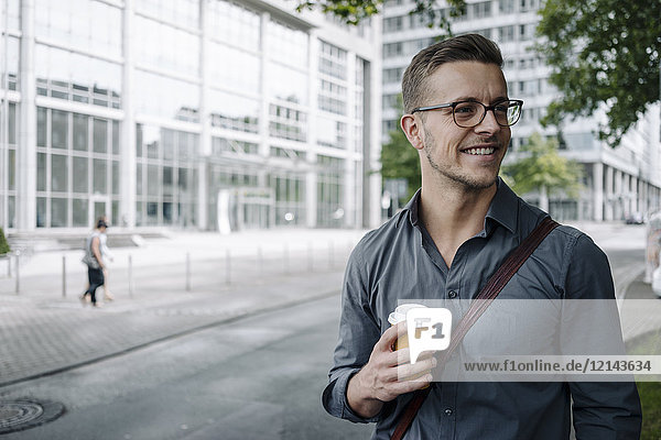 Porträt eines lächelnden jungen Geschäftsmannes mit Kaffee zum Mitnehmen