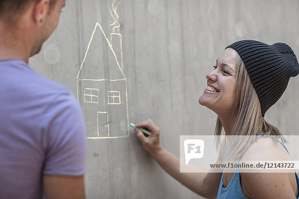 Mann und Frau zeichnen ein Haus mit Kreide auf Betonwand