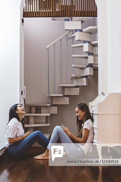 Two happy young women with cell phones sitting on the floor at home
