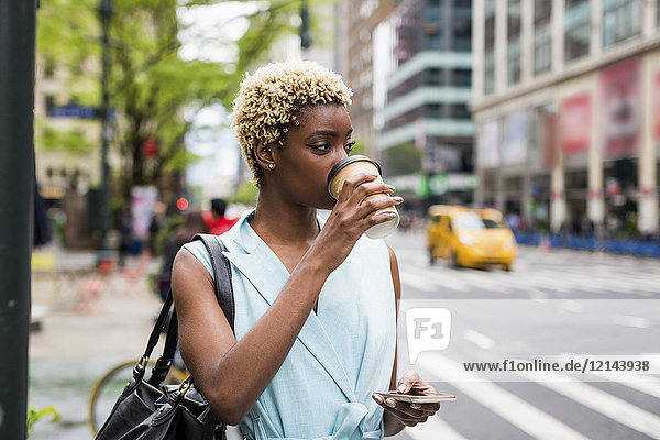 USA  New York  young blonde african-american woman with coffee mug and smart phone