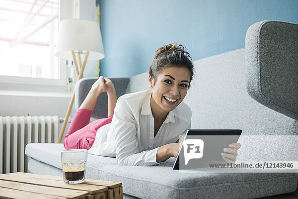 Portrait of laughing woman relaxing on couch with tablet