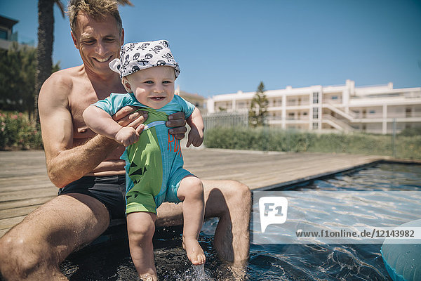 Father and baby son testing water in swimming pool during summer vacation