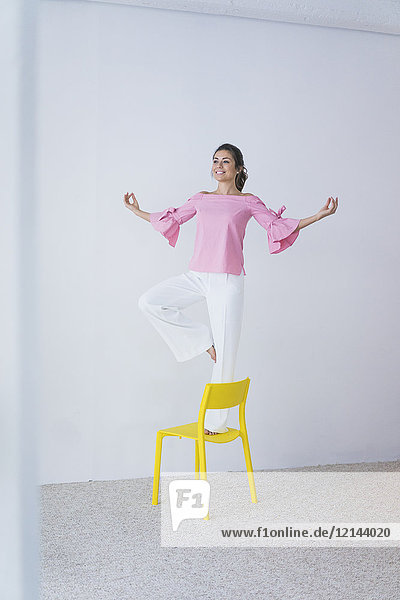Fröhliche junge Frau steht auf gelbem Stuhl und macht Yoga-Übungen