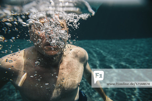 Mann macht Luftblasen unter Wasser in einem Schwimmbad