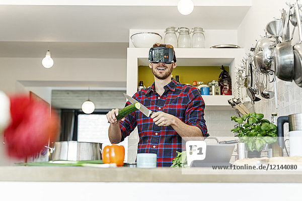 Glücklicher junger Mann mit VR-Brille beim Kochen in der Küche