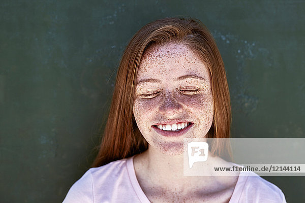 Porträt einer lächelnden jungen Frau mit Sommersprossen  die die Augen schließen.