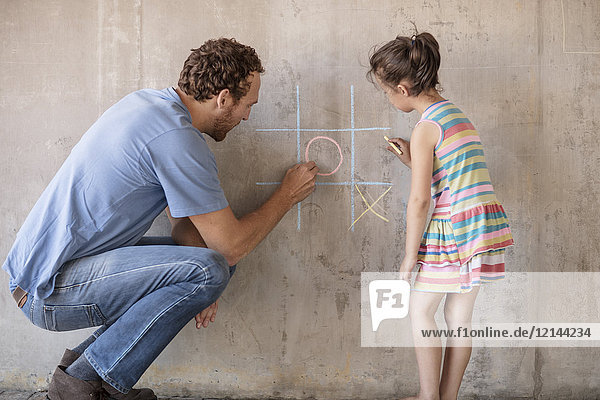 Vater und Tochter spielen tic tac toe mit Kreide auf einer Betonwand