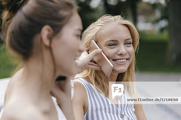 Zwei glückliche junge Frauen mit Handy im Freien