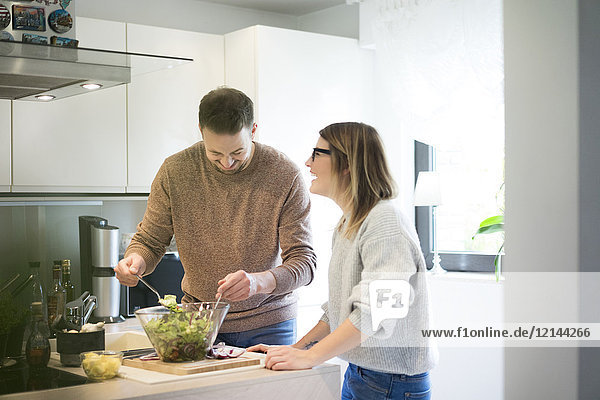 Happy couple preparing salad in kitchen together