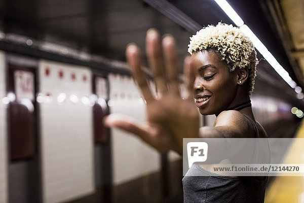 USA  New York City  Porträt einer lachenden Frau auf dem Bahnsteig der U-Bahn-Station mit erhobener Hand