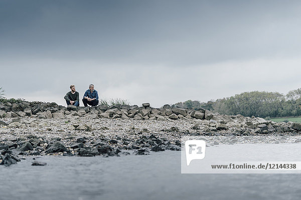 Vater und Sohn sitzen am Fluss und reden miteinander.