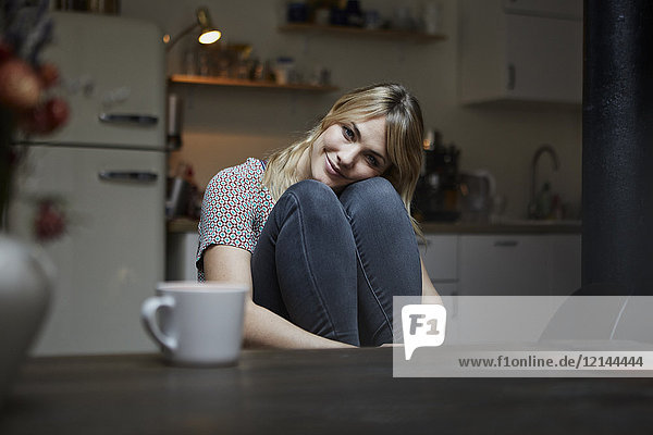 Porträt einer lächelnden Frau,  die in der Küche sitzt.