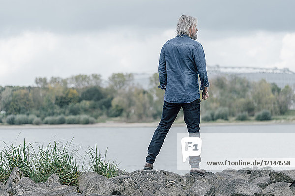 Älterer Mann auf Steinen stehend mit Blick auf den Rhein